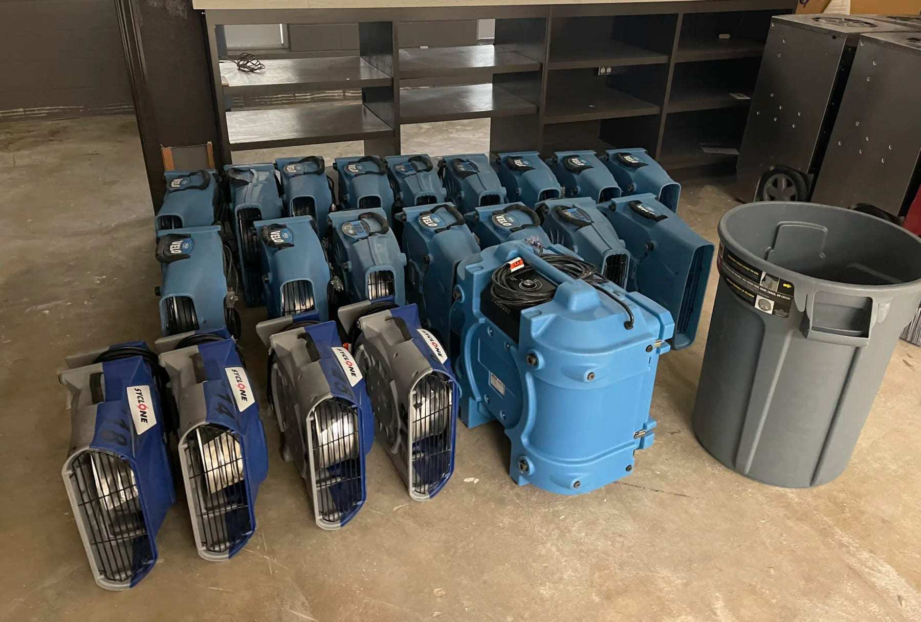 Rows of air movers and dehumidifiers staged in an empty commercial space