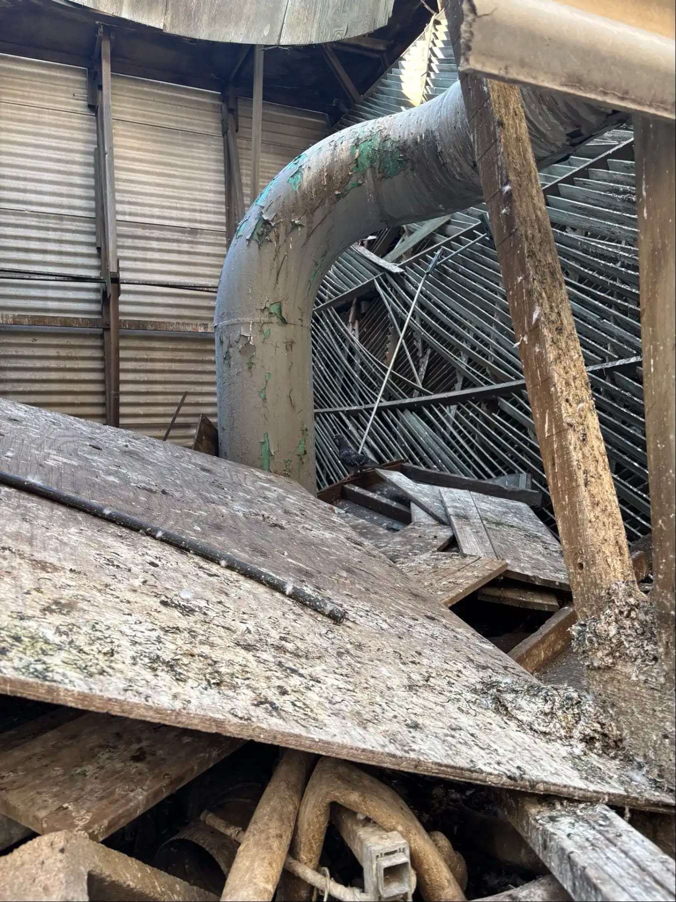 Collapsed ductwork and debris coated in dust inside a warehouse