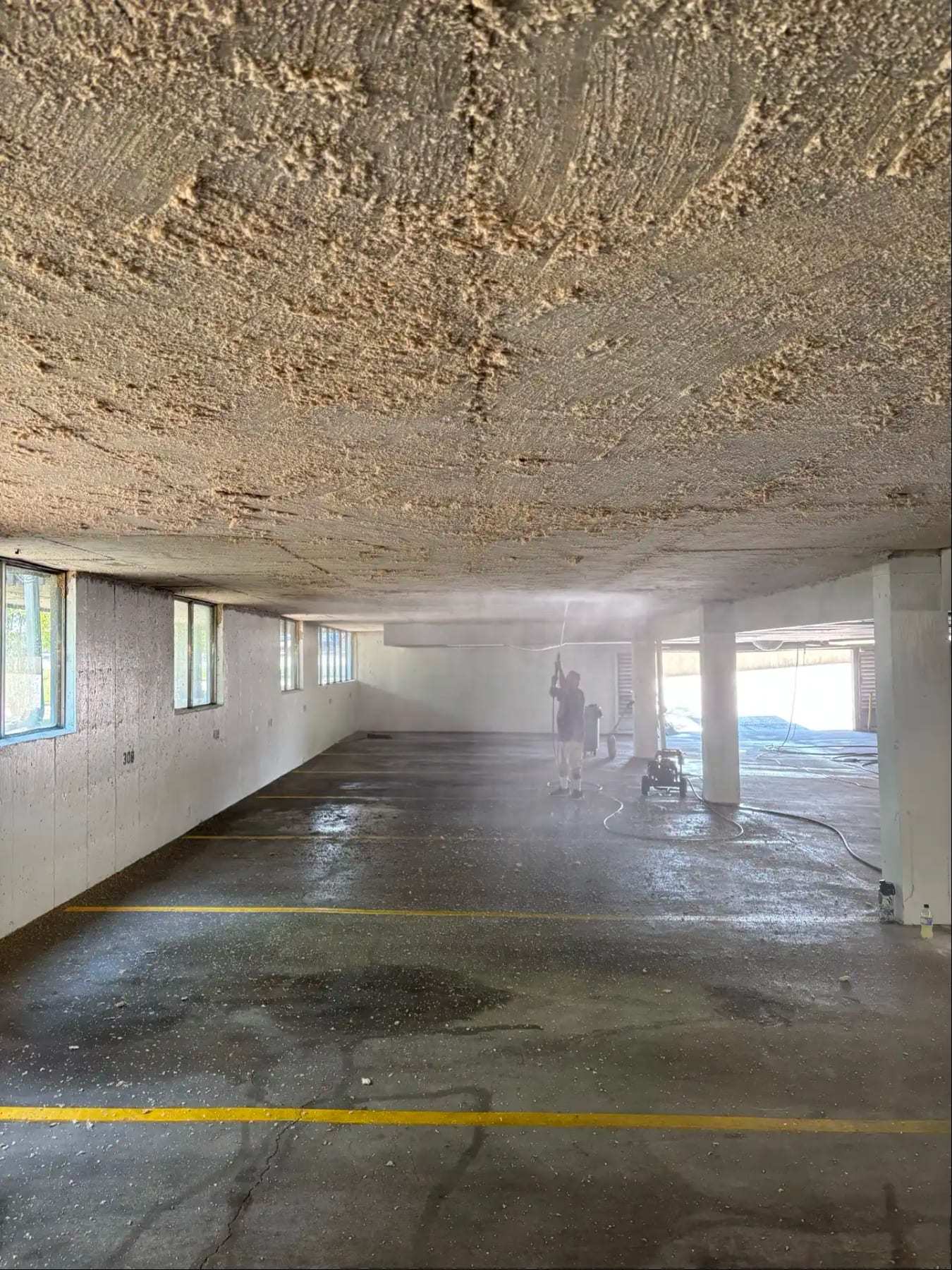 Wet floor of a parking garage with standing water along the stalls